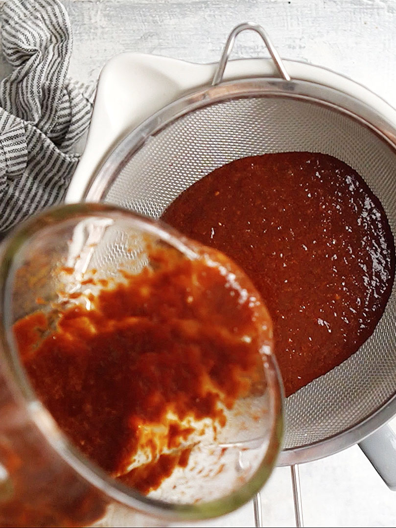 Pouring red sauce to a mesh strainer over a bowl.