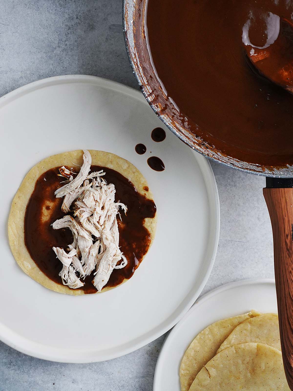 A corn tortilla with mole sauce and shredded chicken on the middle of the tortilla.