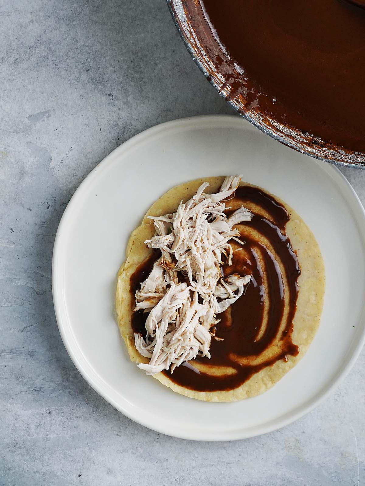 A corn tortilla with mole sauce and shredded chicken on one side of the tortilla.