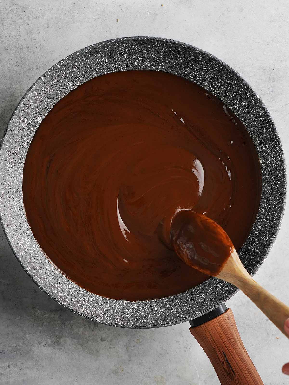 A gray skillet with mole sauce and a wooden spoon stirring it.
