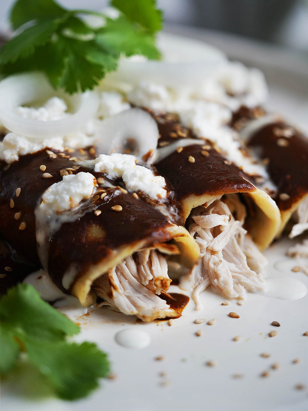 Three mole enchiladas on a white plate topped with sesame seeds, queso fresco and onion slices.