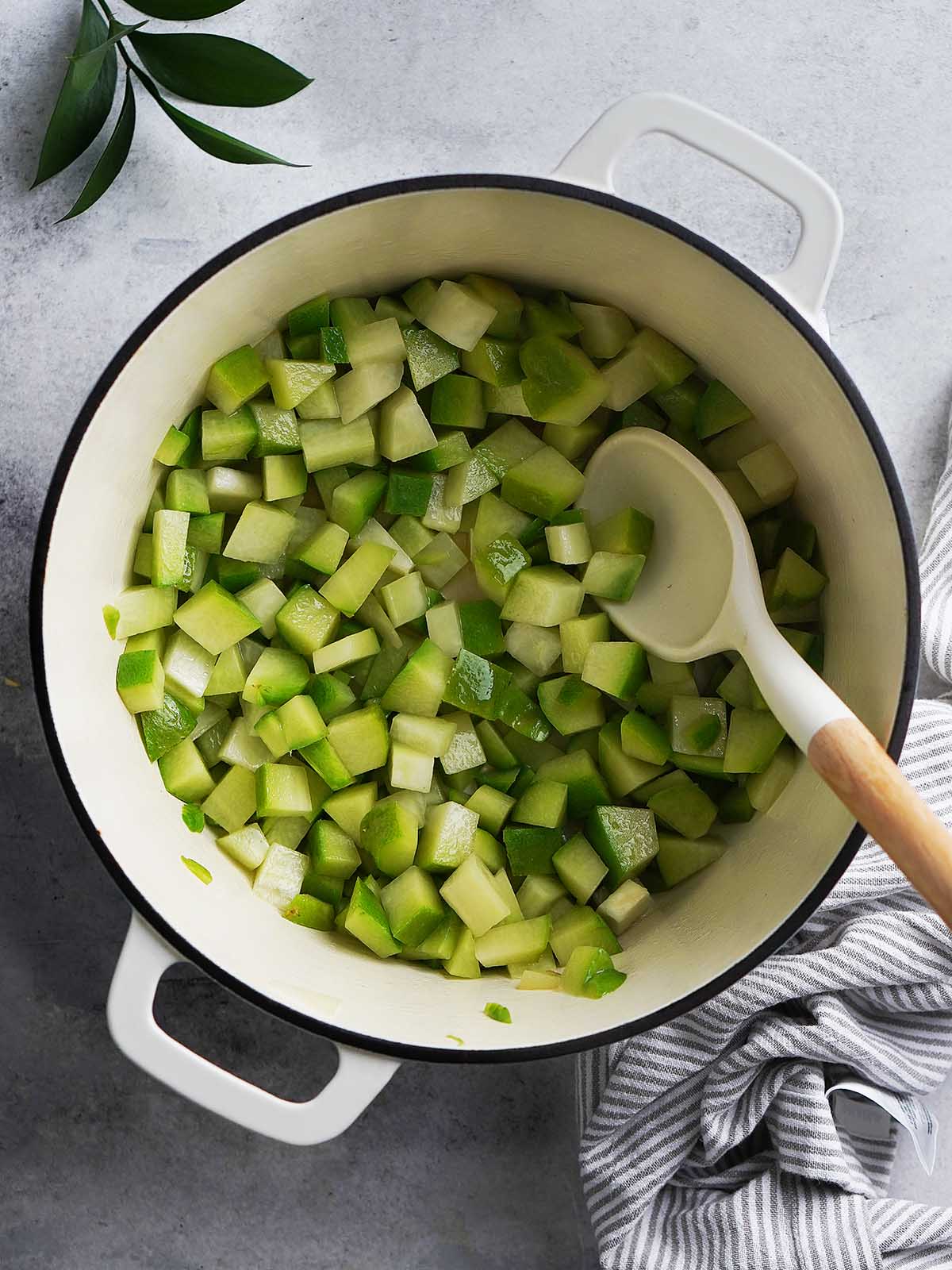 Sauteing chayote chunks in a white pot.