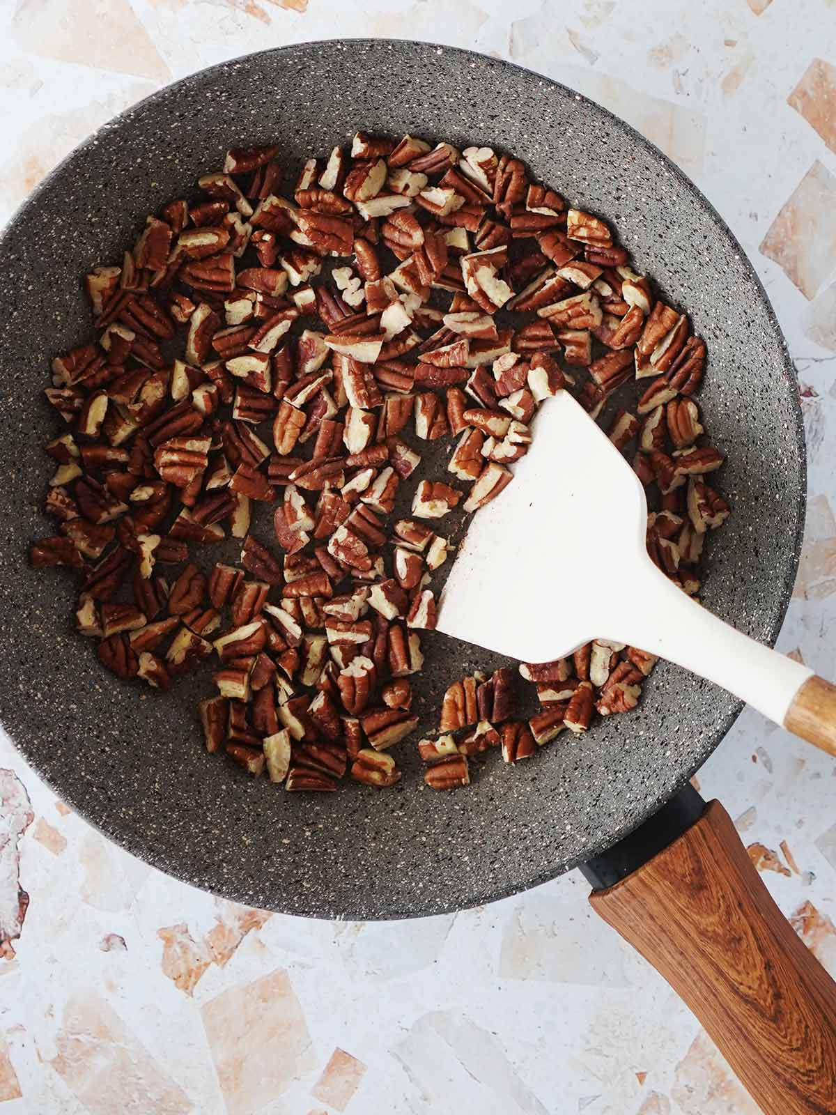 Toasting chopped pecans on a gray skillet.