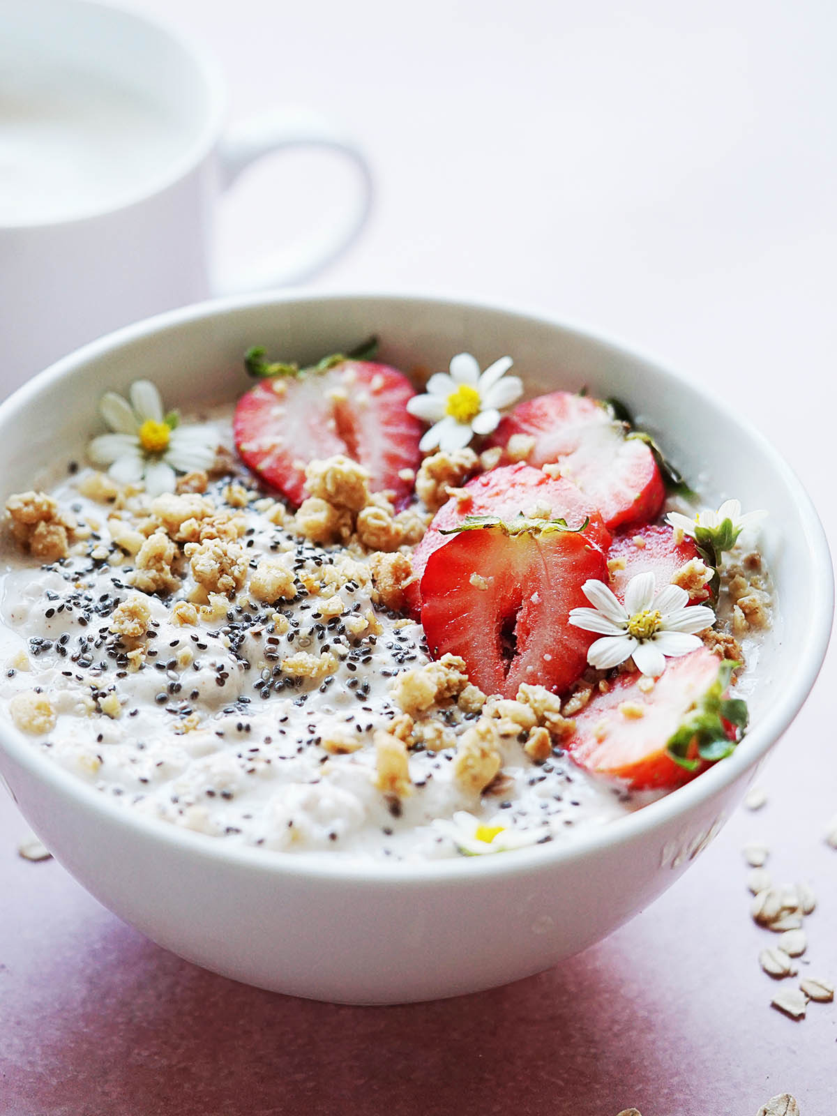 A white bowl with oatmeal and yogurt topped with chia seeds and strawberries.