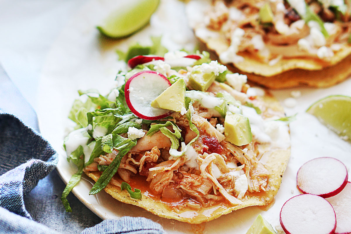 Two tinga tostadas on a plate garnished with lettuce and slices of radishes.