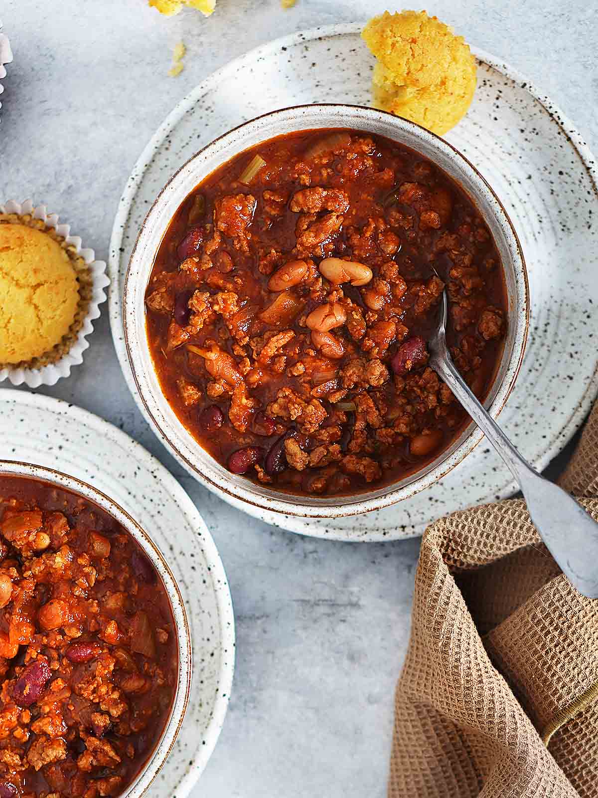 Two white bowls of chili with cornbread muffins on the side.