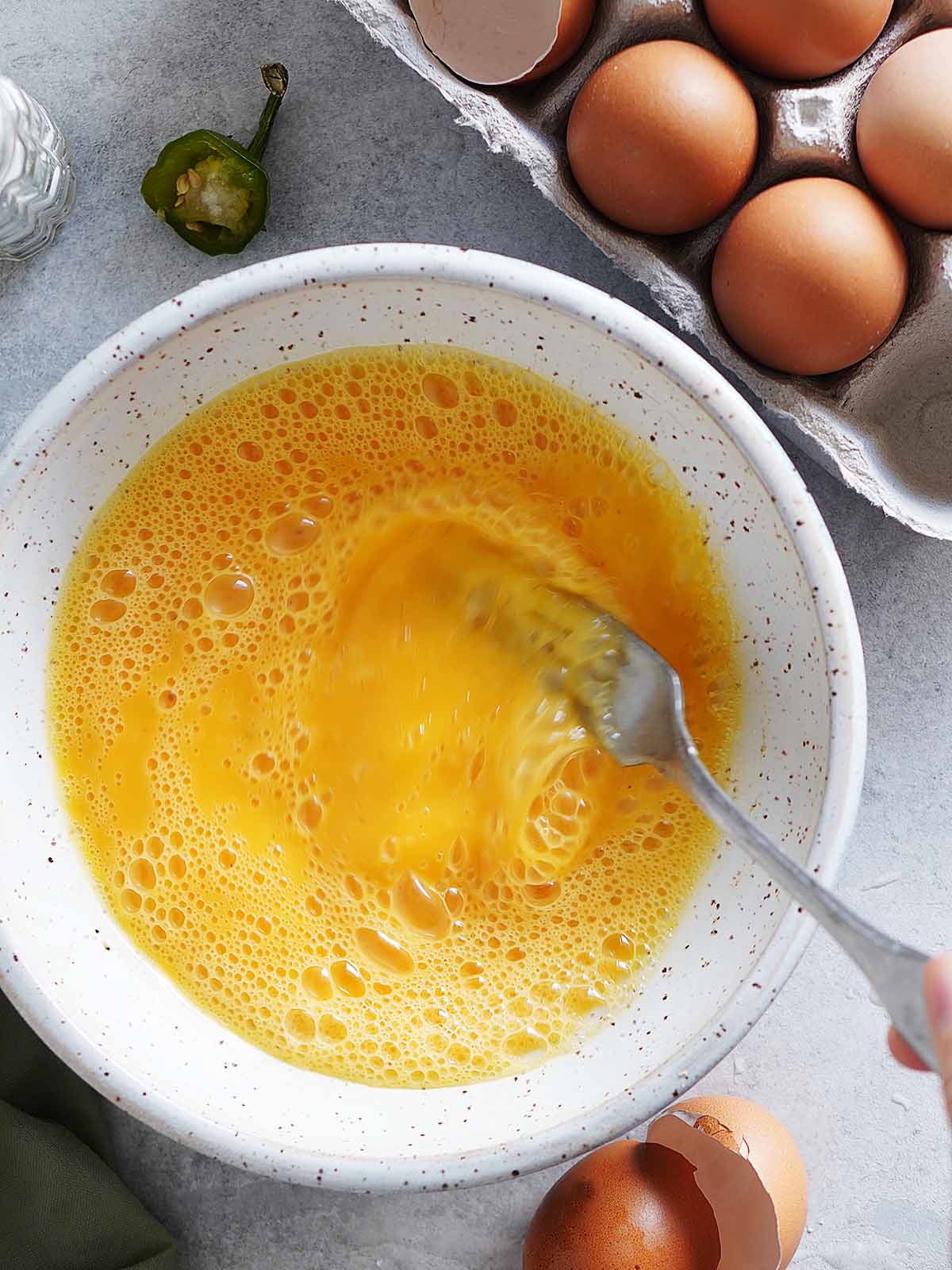 Scrambling eggs with a fork in a white bowl.