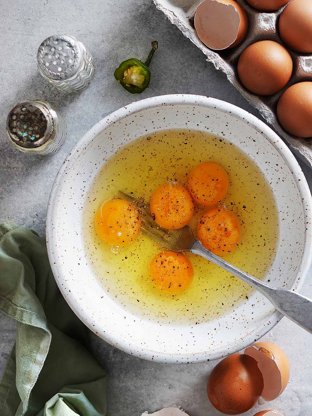 Five eggs inside a bowl sprinkled with salt and pepper.