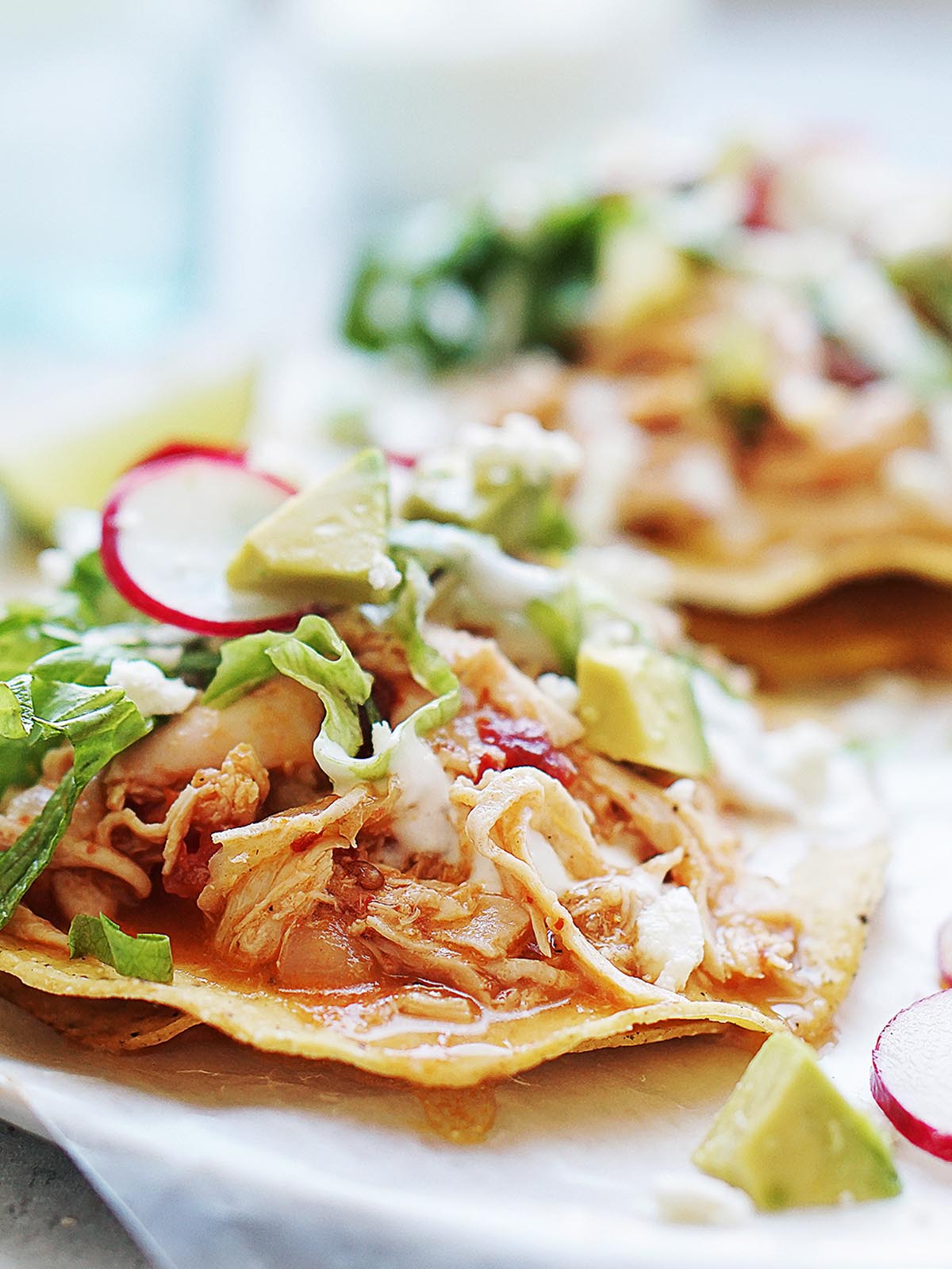 Two tinga tostadas on a plate garnished with lettuce and slices of radishes.