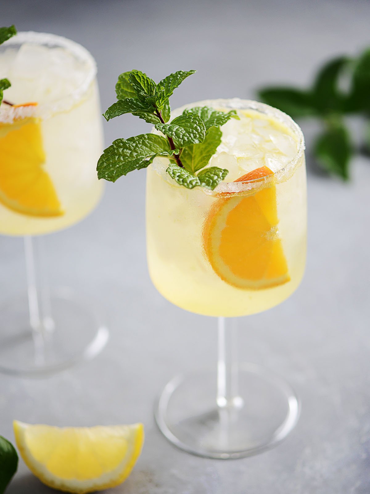 Two cocktail glasses with vodka collins garnished with an orange slice and a mint sprig.