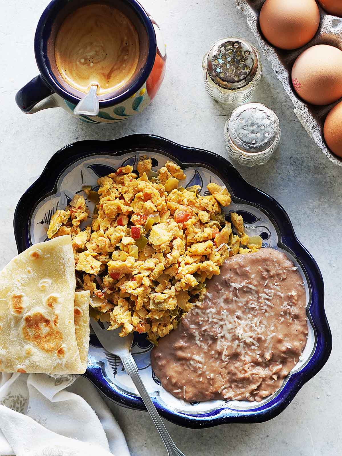 Huevos a la mexicana on a blue plate with refried beans and a tortilla on the side.