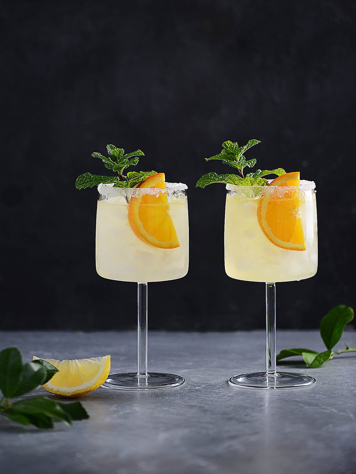 A cocktail glass with vodka collins garnished with an orange slice and a mint sprig.