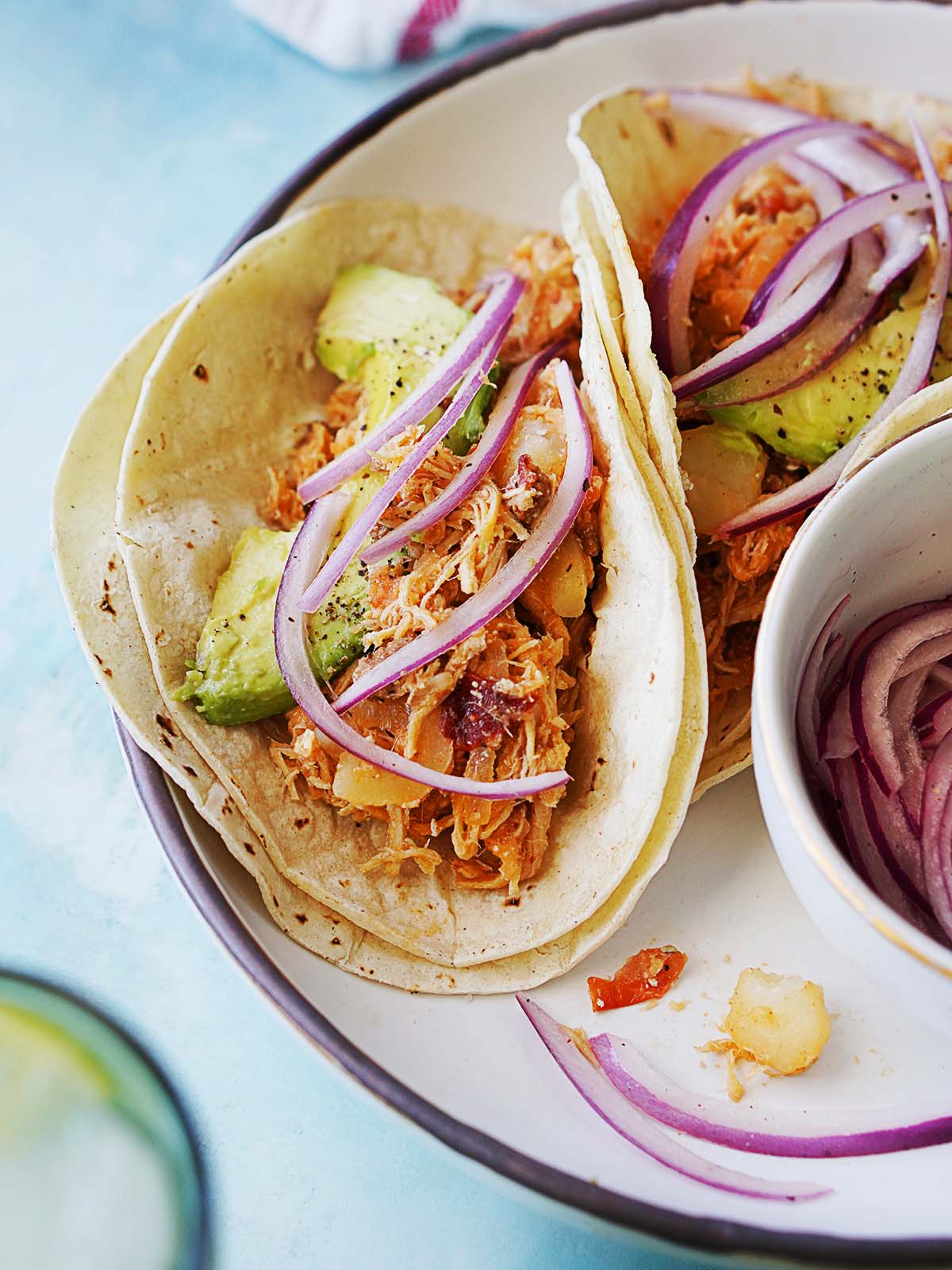Two tinga tacos on a plate garnished with pickled onions.
