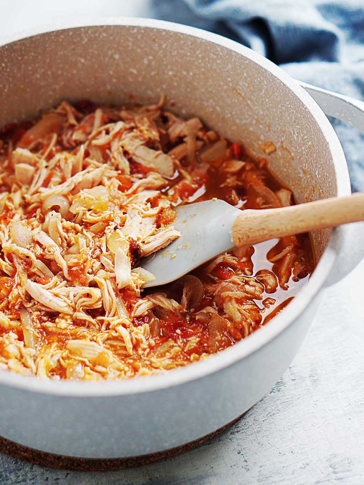 A medium saucepan with shredded chicken in a tomato and onions sauce.