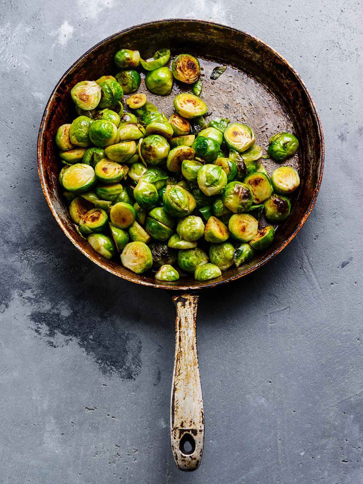 Fried Brussels sprouts in frying pan on concrete background