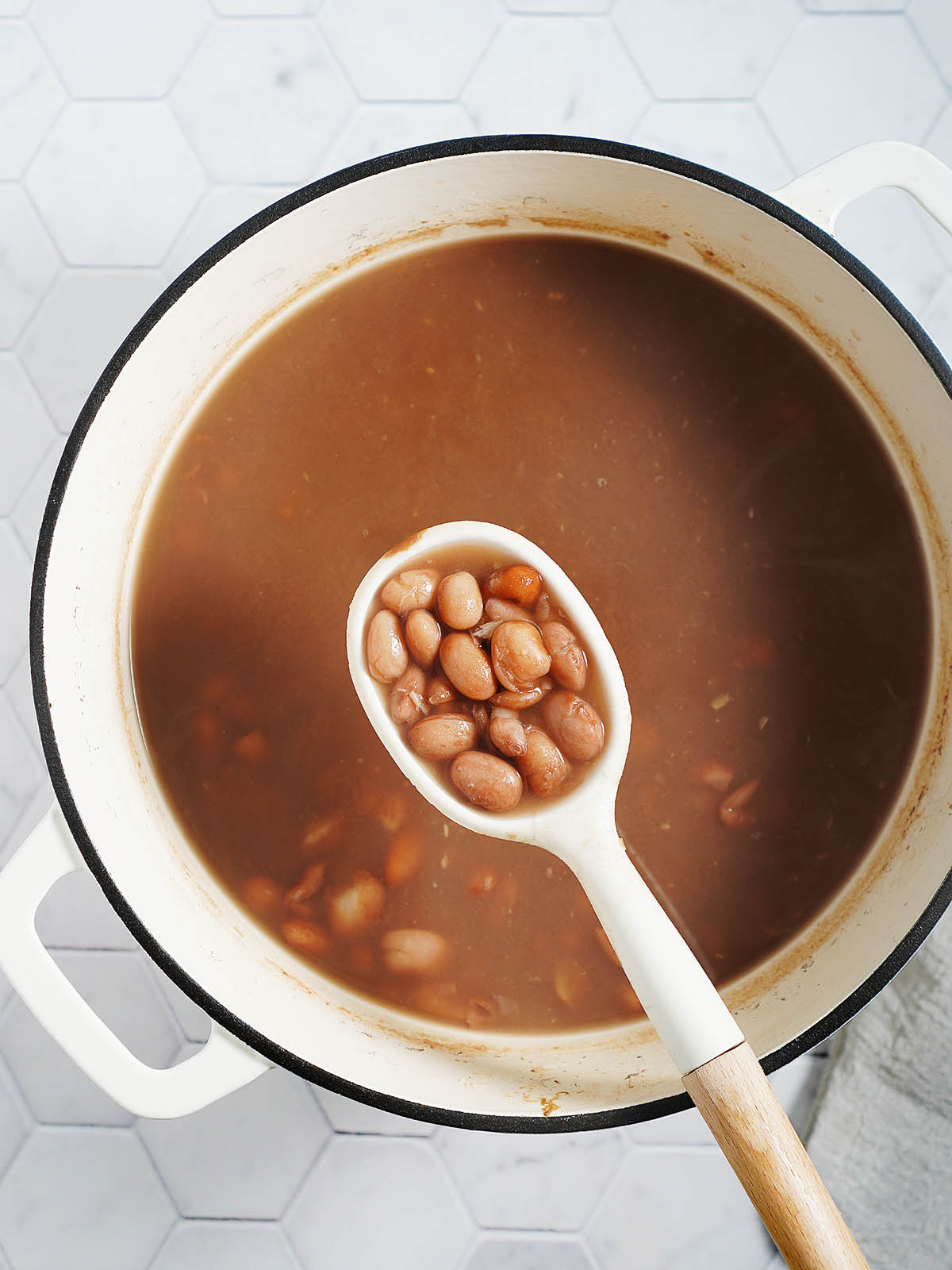 A pot with cooked beans and a white spoon holding some beans.