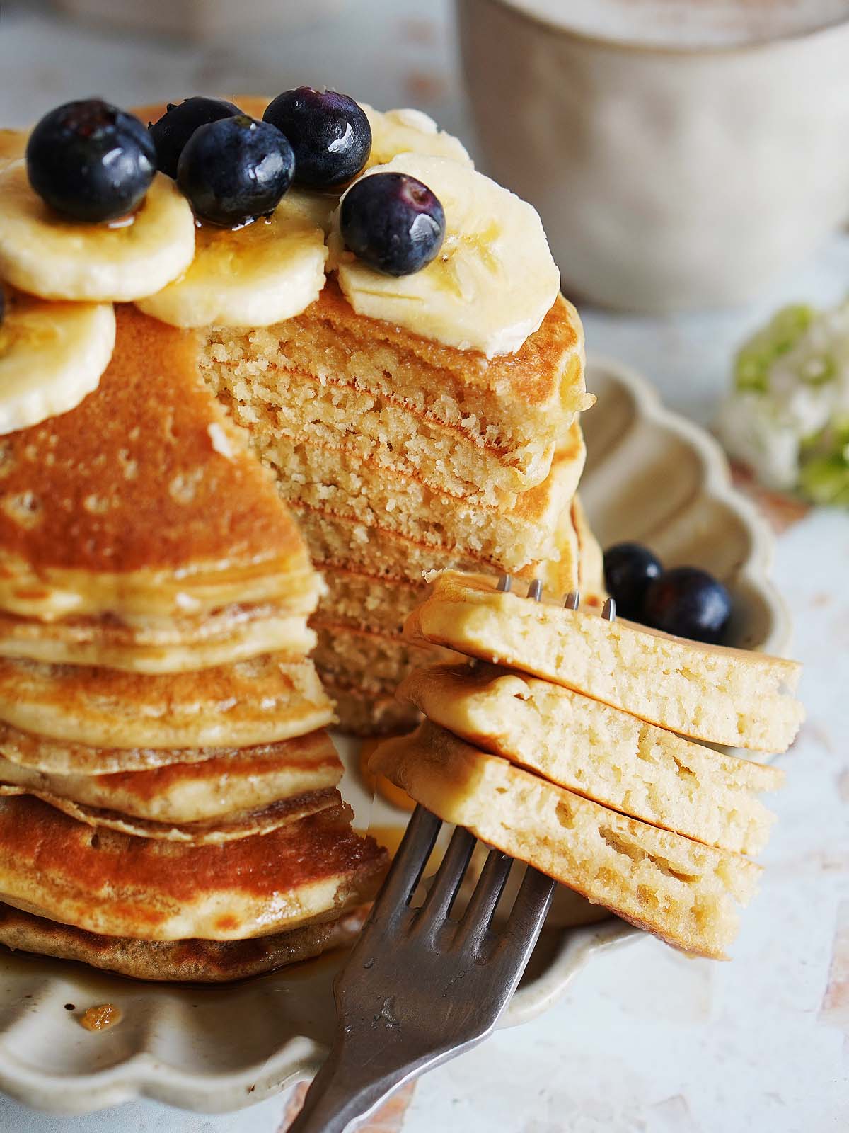 A stack of hotcakes topped with sliced bananas and blueberries.