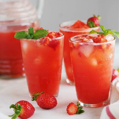 Three glasses with ice and strawberry water topped with small chunks of strawberries and the jar in the background.