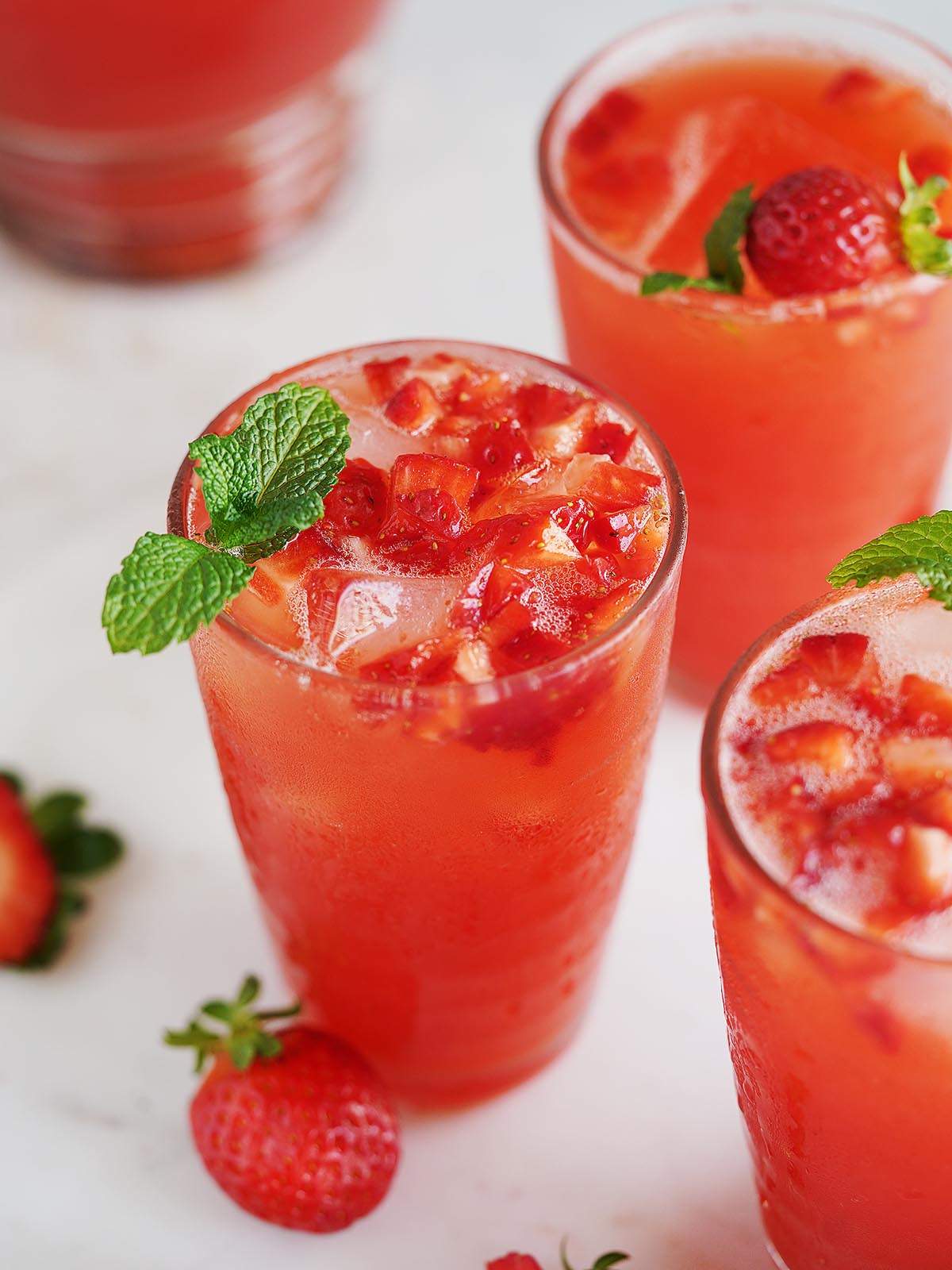 Three glasses with ice and strawberry water topped with small chunks of strawberries.