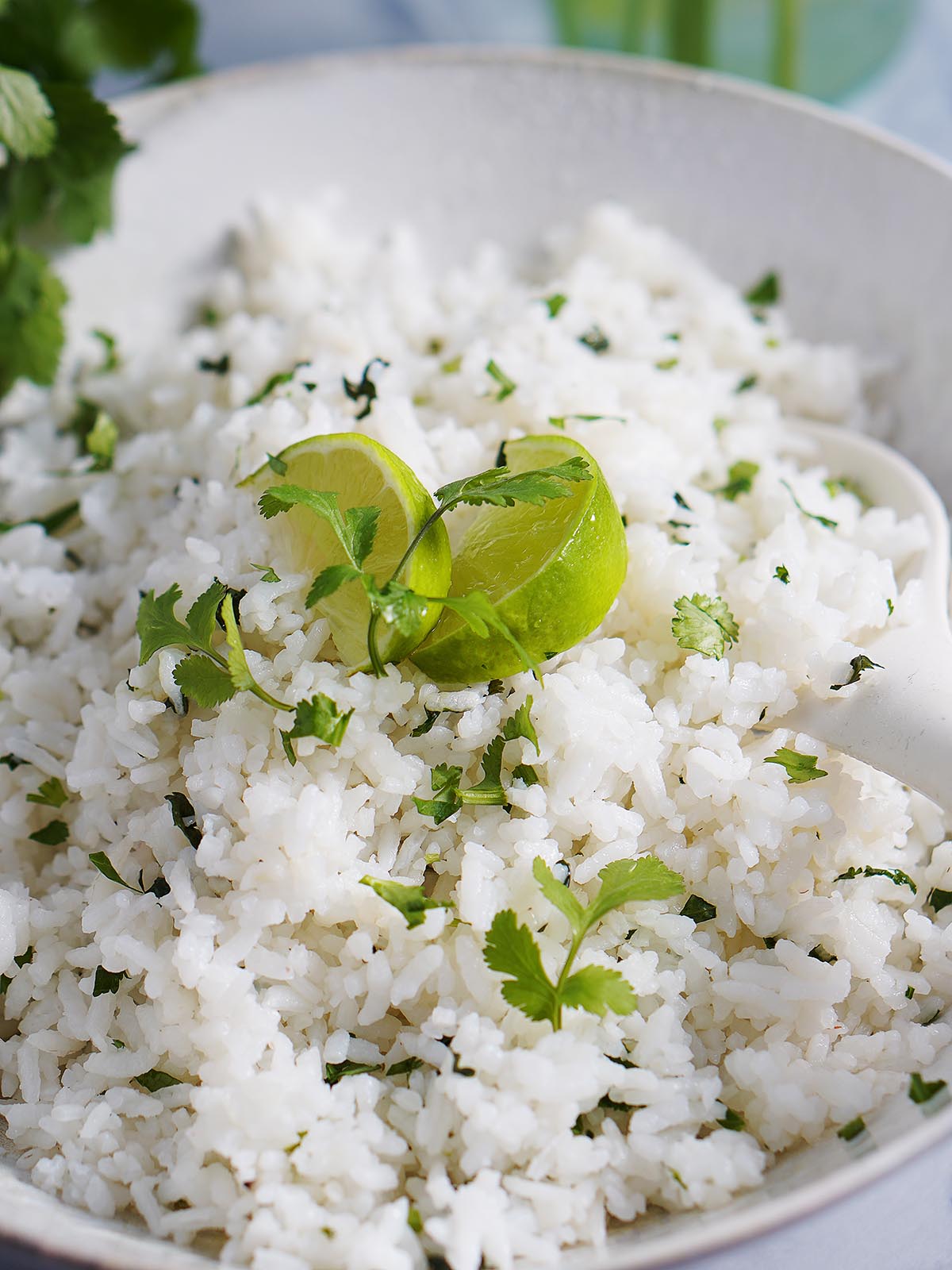 A white bowl with cilantro lime rice garnished with slices of lime and cilantro sprigs.