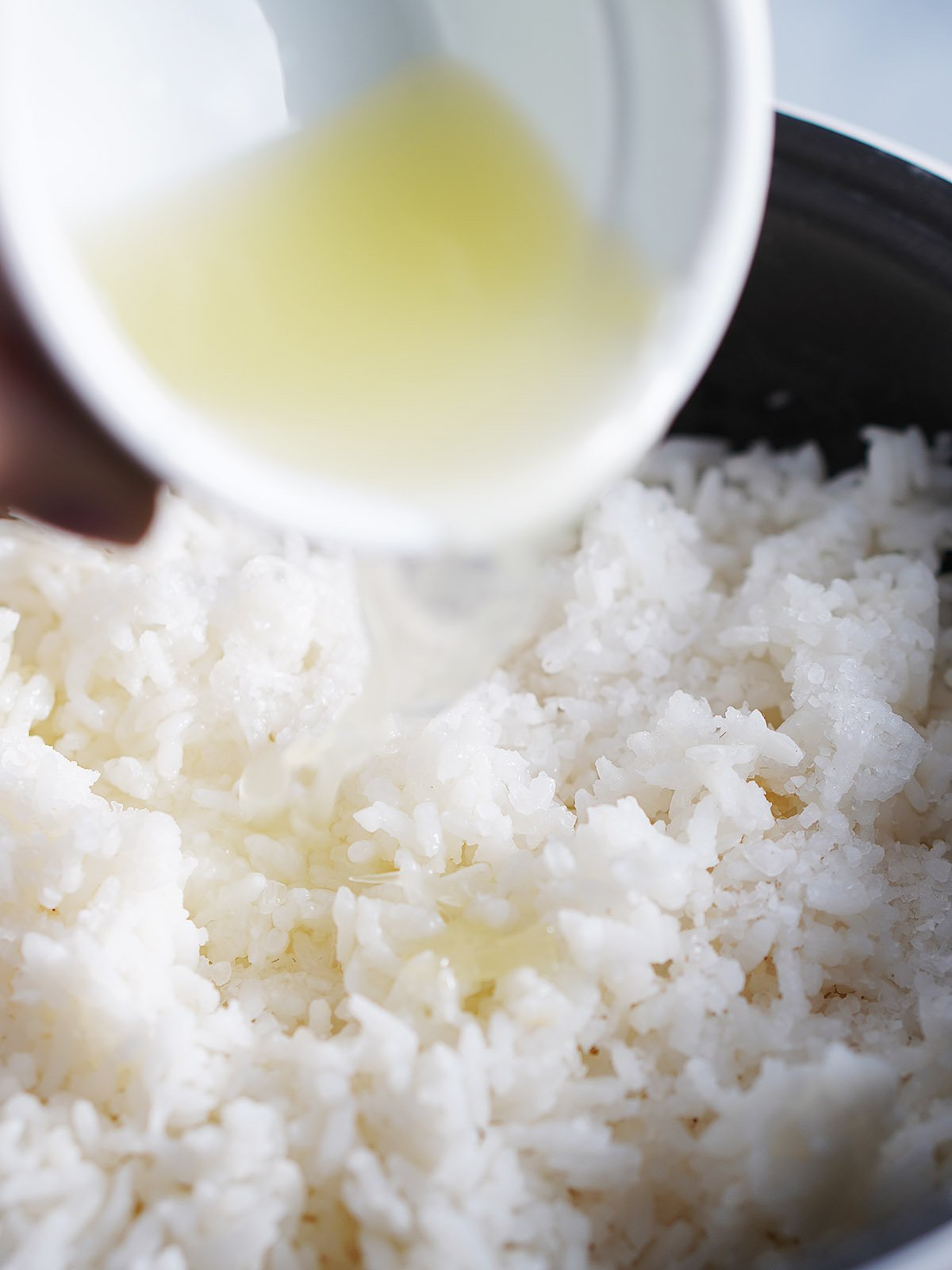 Adding lime juice to a rice cooker pot with cooked white rice.