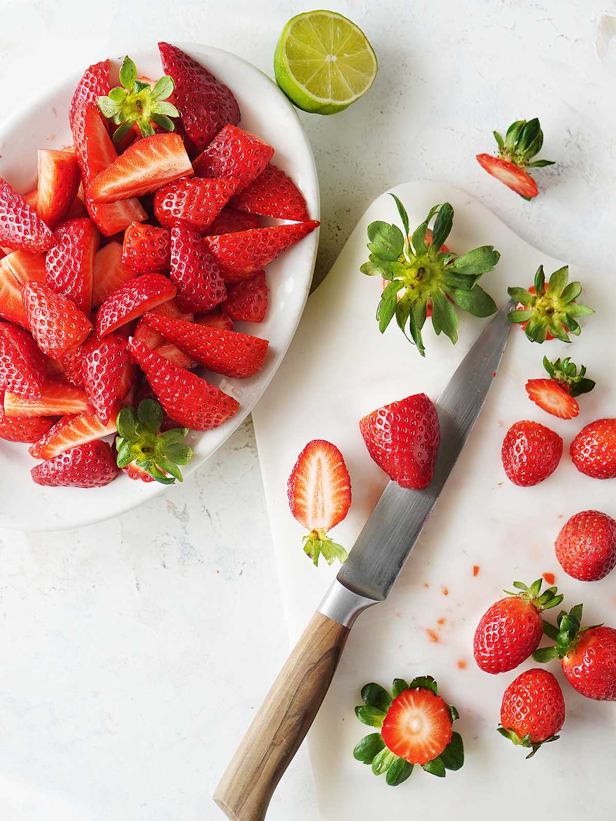 Cutting strawberries on a white cutting board.