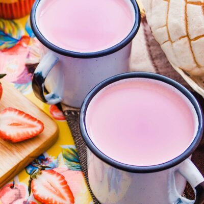 Strawberry Atole de fresa in two white mugs with Mexican bread and strawberries on the side.