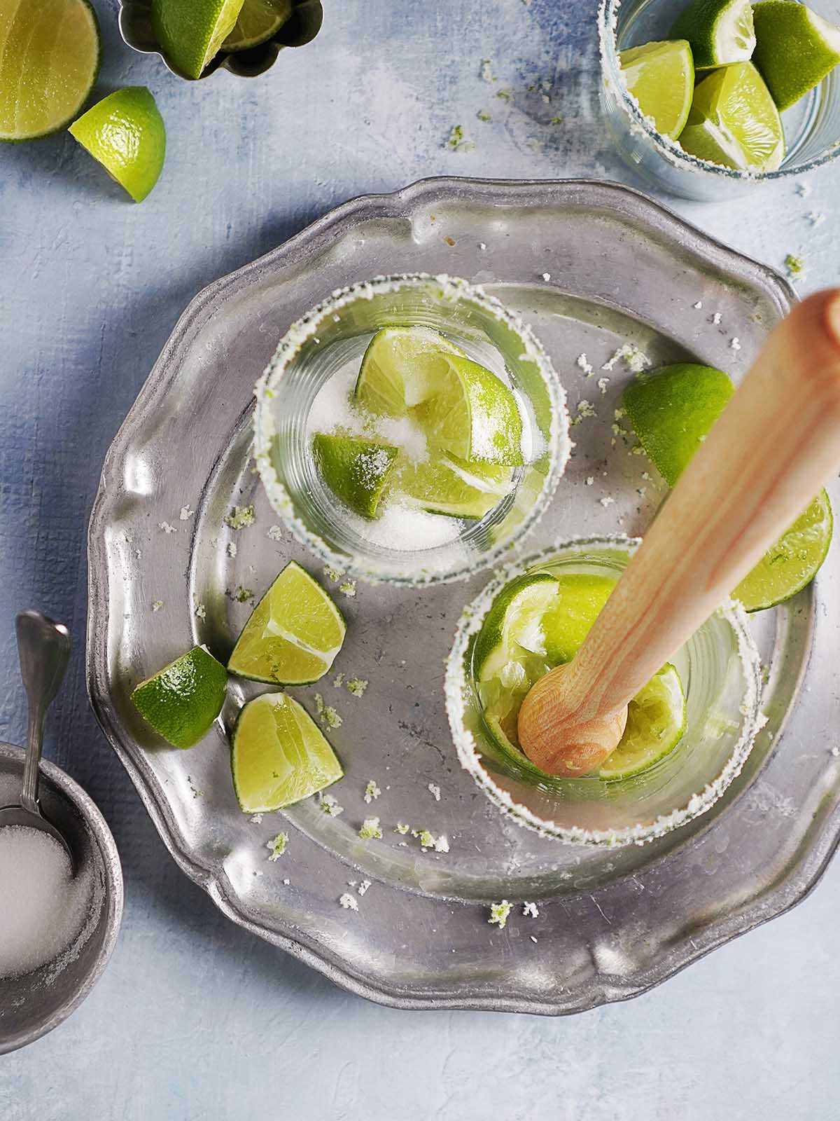 Crushing cut fresh limes with the sugar in a cocktail glass.