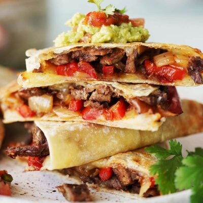 A stack of carne asada quesadillas cut in triangles top with a dollop of guacamole.