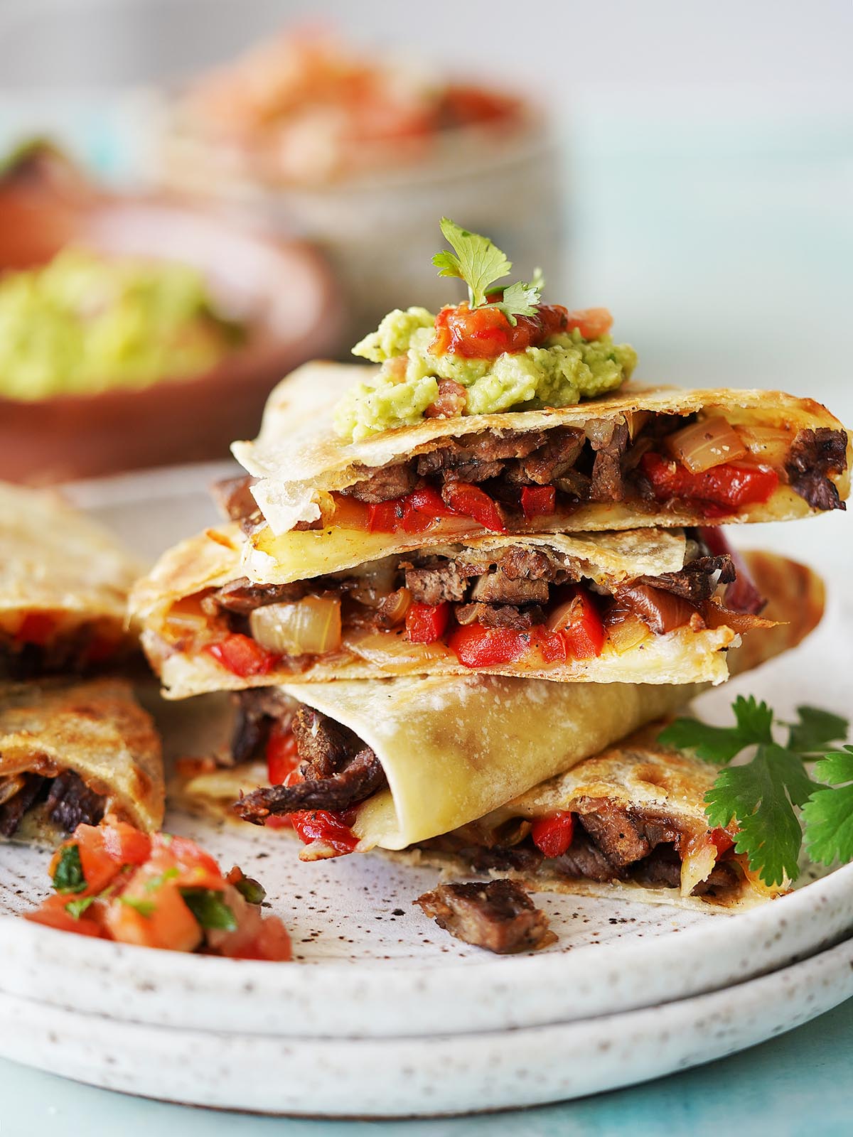 A stack of carne asada quesadillas cut in triangles top with a dollop of guacamole.