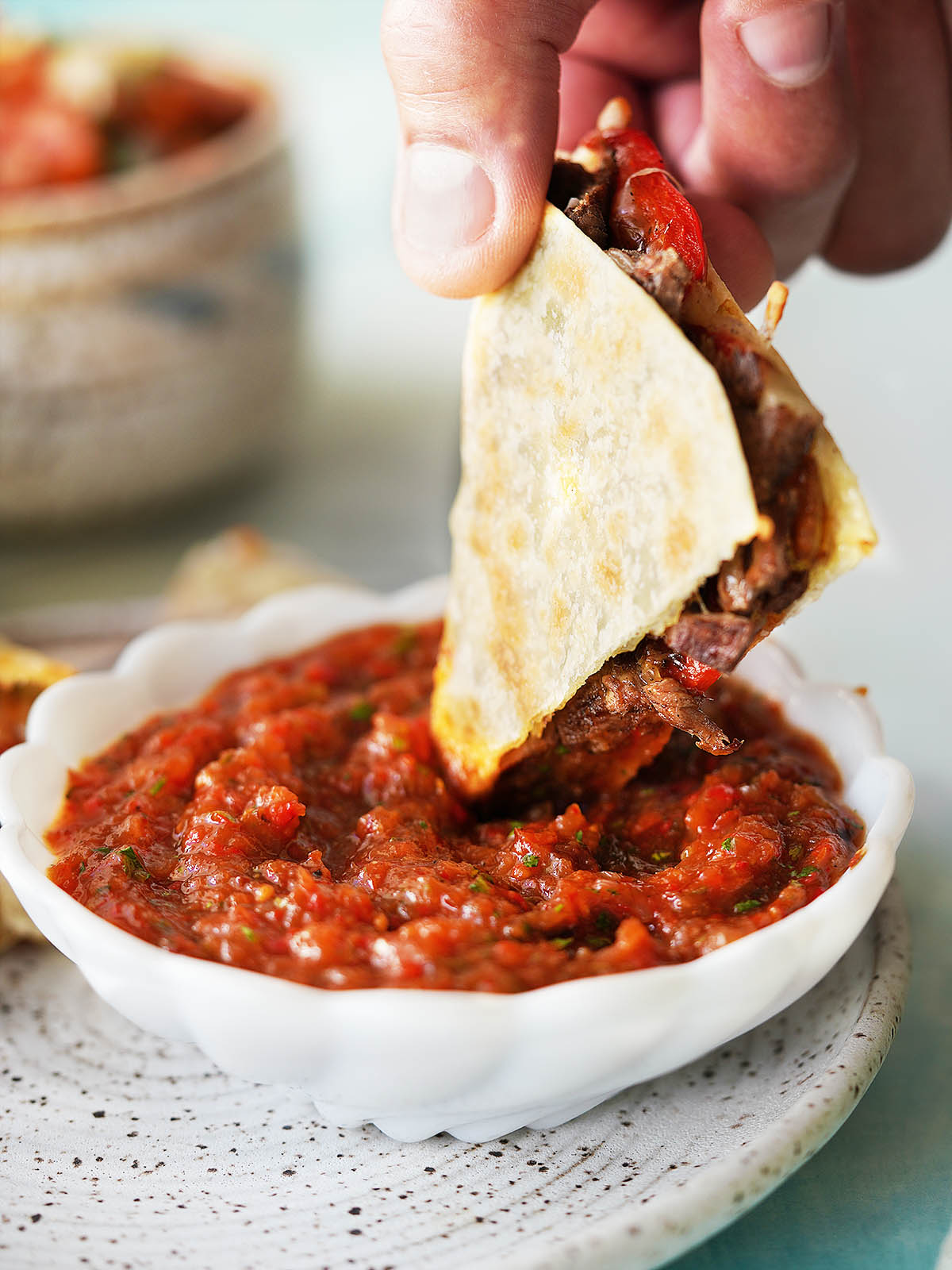 A hand dipping a slice of quesadilla into roasted salsa.