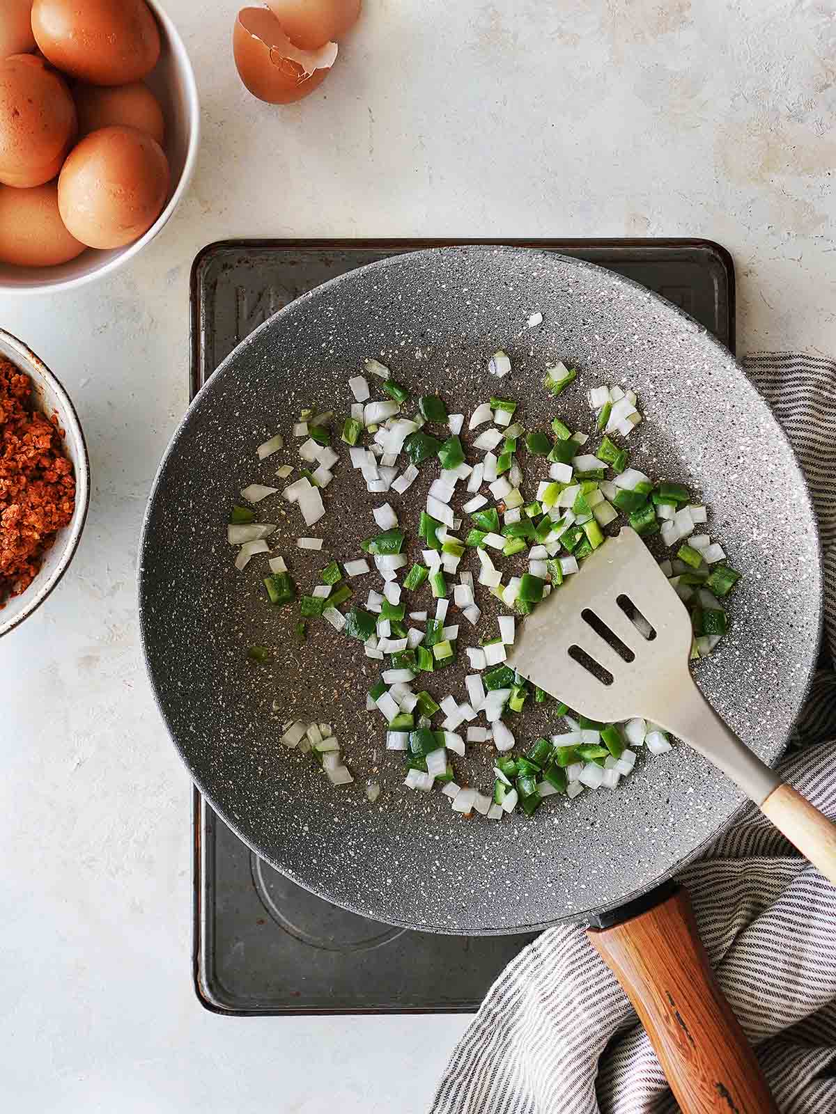 A skillet with chopped onions and jalapeños with a spatula.