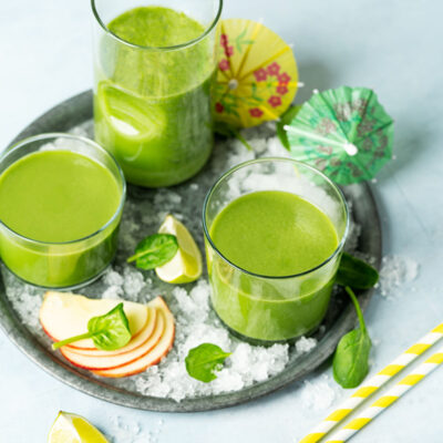 Jugo Verde in glass with organic ingredients, vegetables on a light blue background.