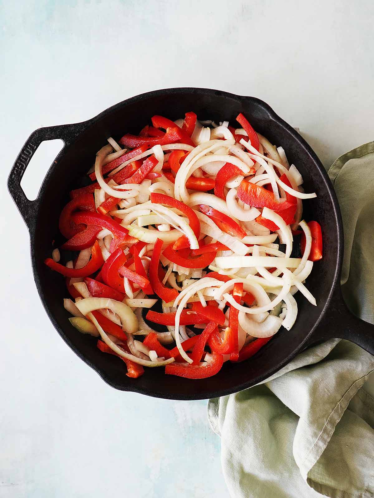 An iron skillet sauteing onions and red bell peppers.