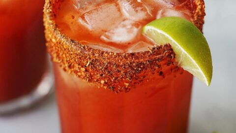 A Michelada glass with ice, garnished with a slice of lime.