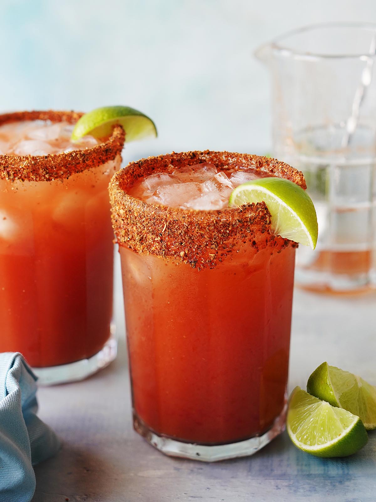 Two Michelada glasses with ice, garnished with a slice of lime.