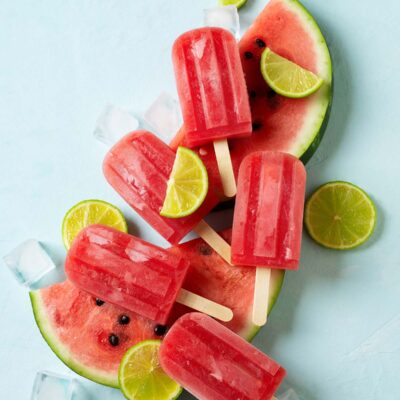 Watermelon popsicle with ice cube and lime on plate, on blue background, top view.