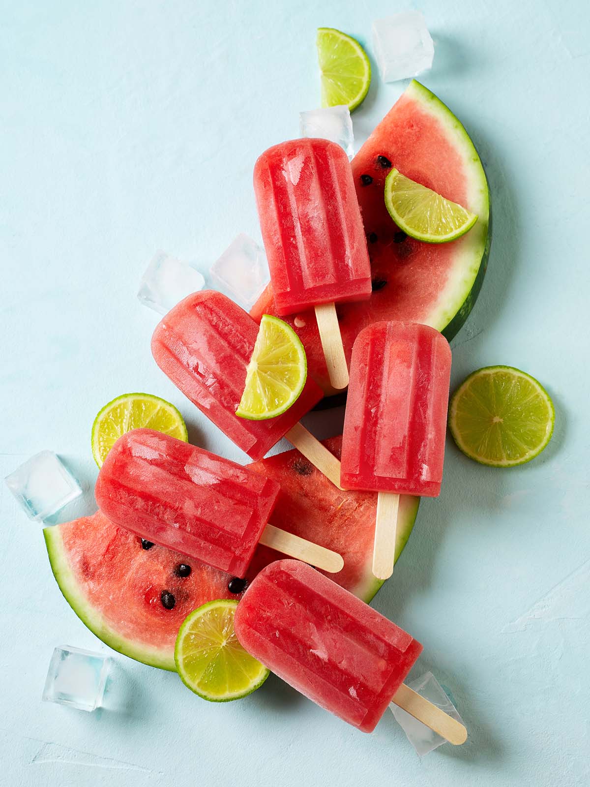 Watermelon popsicle with ice cube and lime on plate, on blue background, top view.
