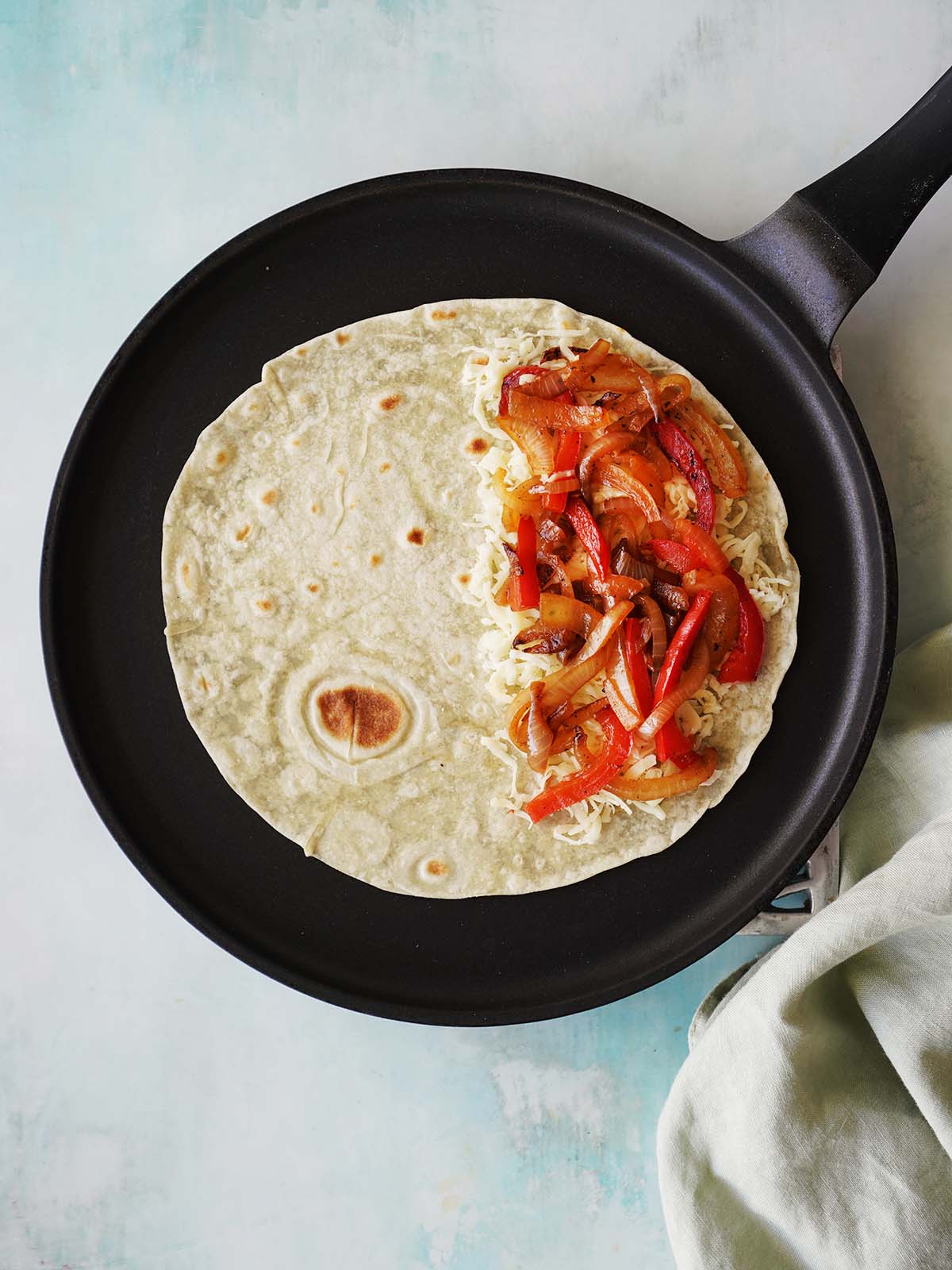 A flour tortilla topped with cheese and sauteed veggies on a skillet.