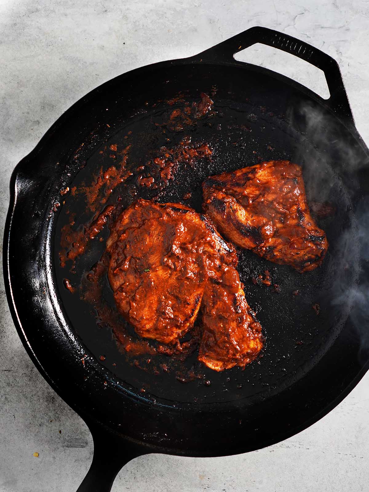Pork fillets in adobo are being cooked in a cast iron skillet.