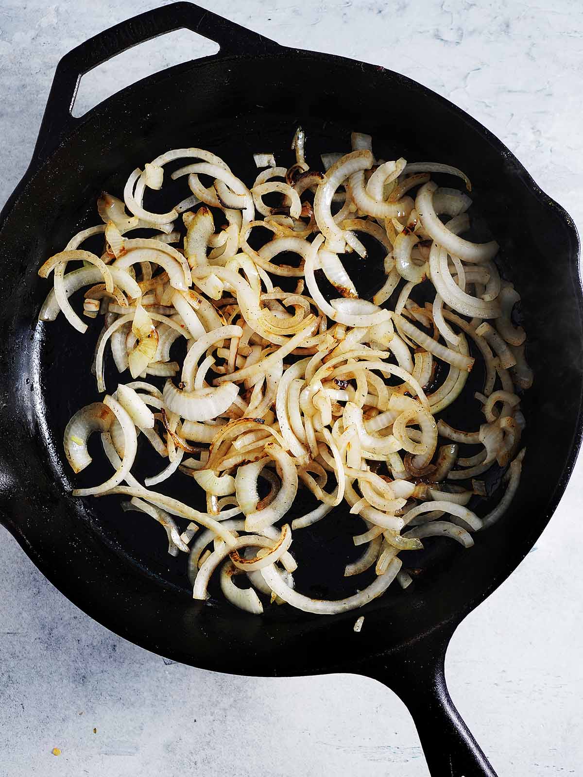 Sliced white onions are being cooked in a cast iron skillet.