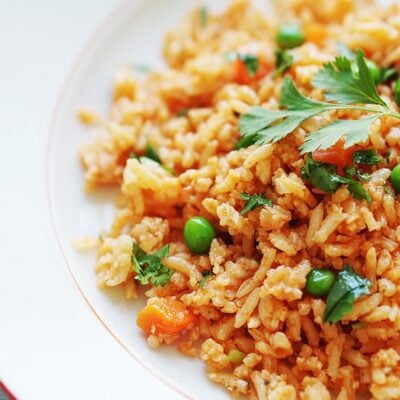 A white plate with red rice garnished with cilantro.
