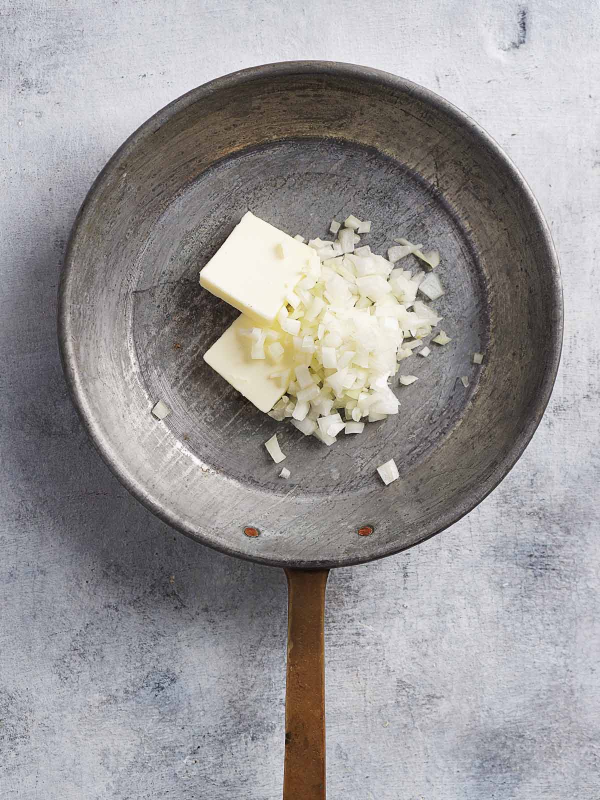 A skillet with butter and chopped white onions.