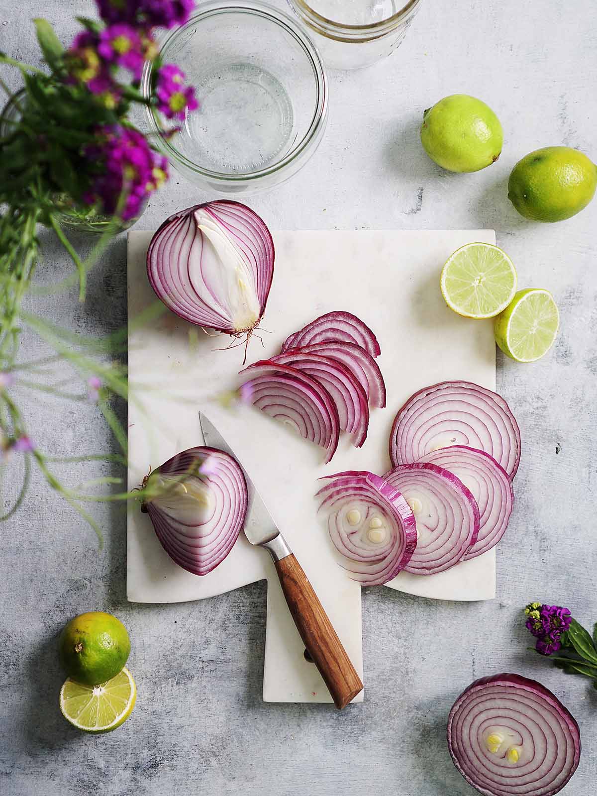 A white cutting board with sliced onions and a knife.