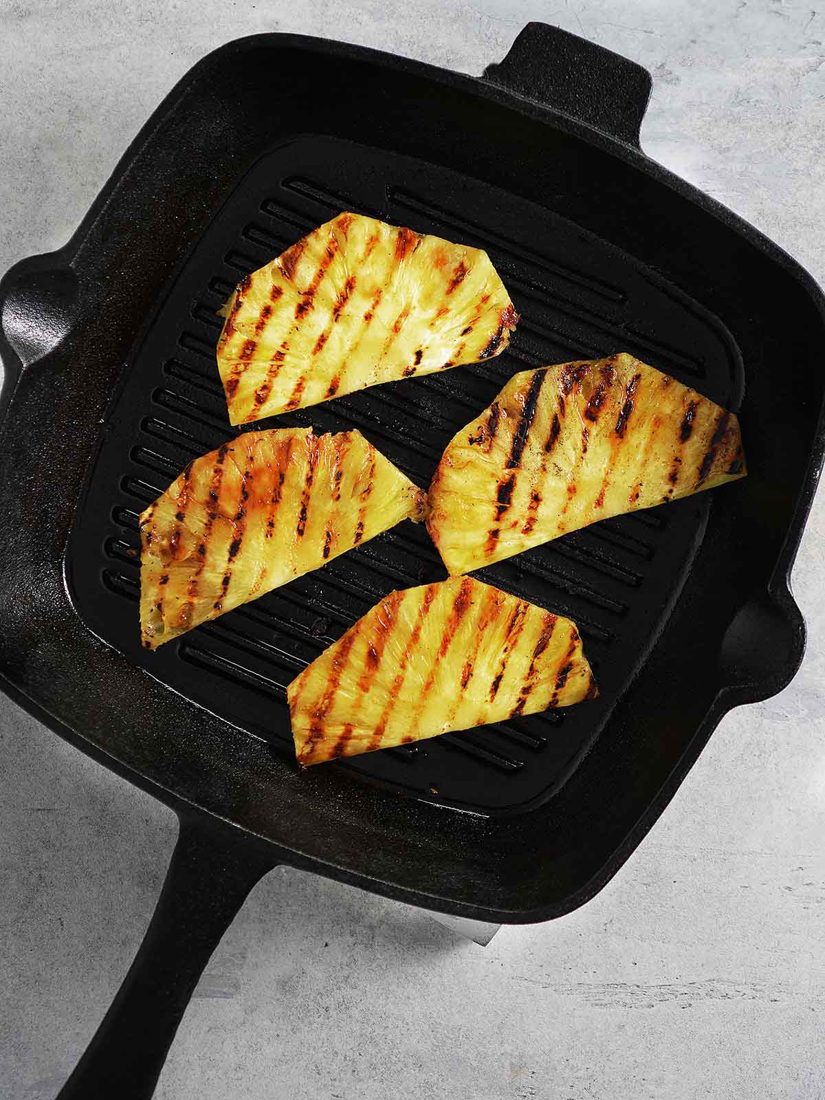 Slices of pineapple being grilled in a cast iron skillet.