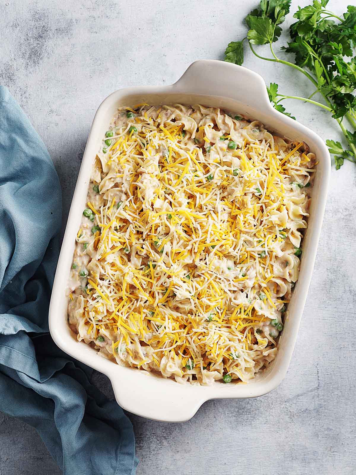 A classic tuna noodle casserole in a rectangular glass baking dish with melted cheese and peas and shredded cheese on top.