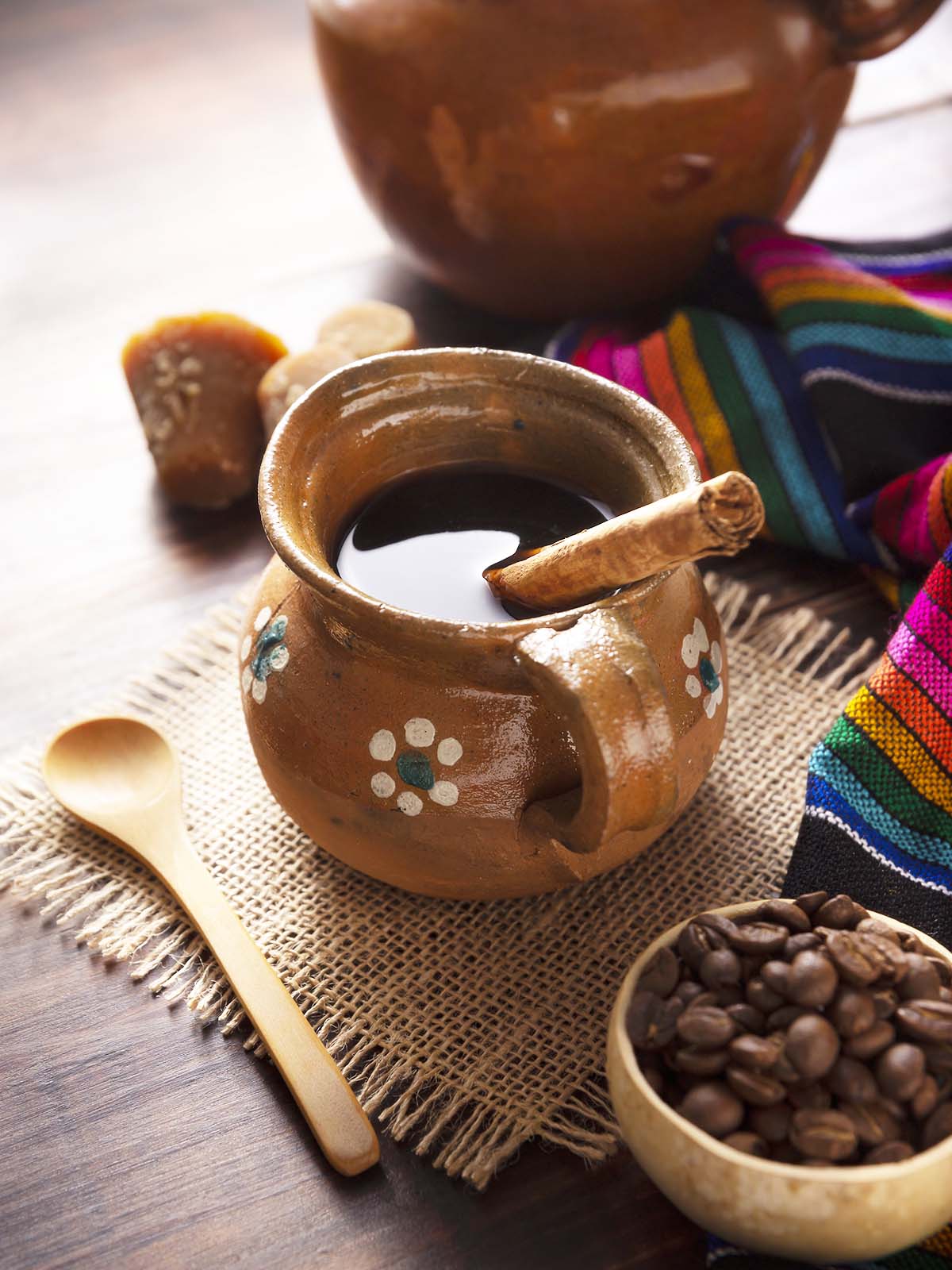 Cafe de Olla and the ingredients: coffee, cinnamon and piloncillo, served in a clay cup called "jarrito" on a rustic wooden surface.