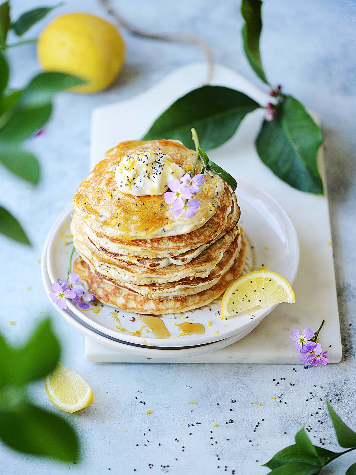 A stack of lemon chia protein pancakes with lemon leaves and a lemon in the background.