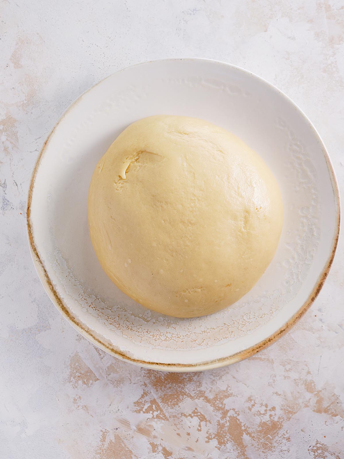 The dough in round shape inside a wide bowl.