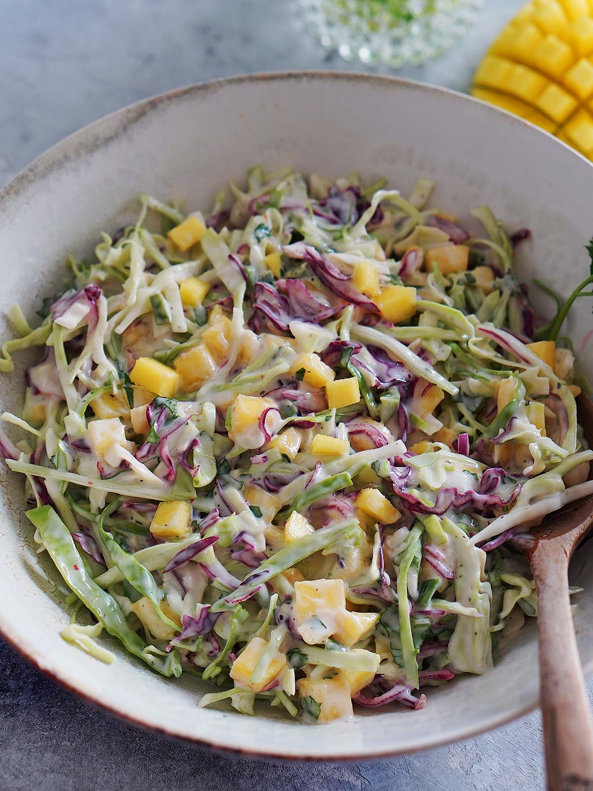 A white bowl with cabbage slaw and a wood spoon.